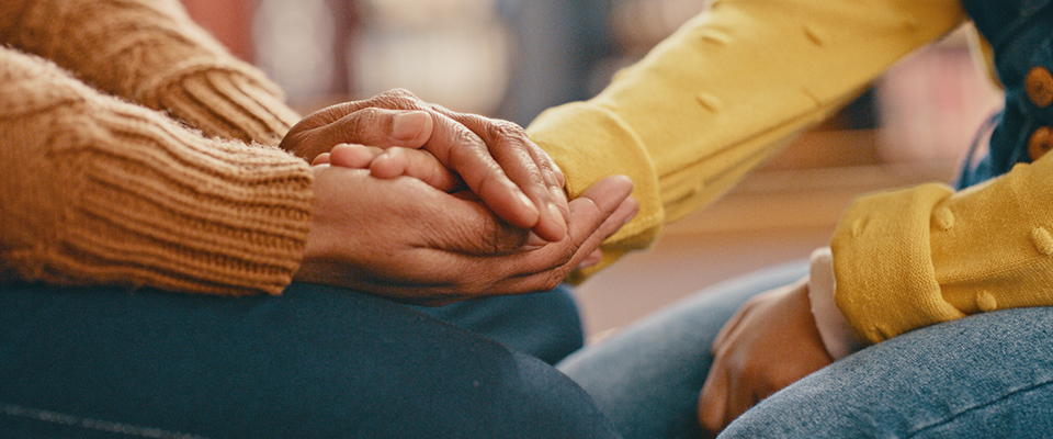 Two people hold hands, one comforting the other, in a display of care